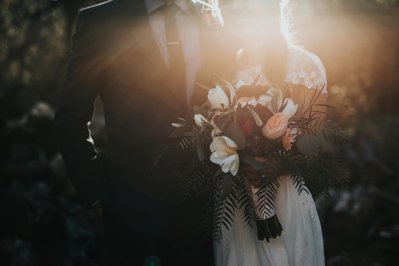 Newlyweds holding a bouquet outdoors in warm sunlight